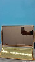 Reflection showing the very mirror-like surface of the larger gold tray with a partially visible hand holding a phone.
