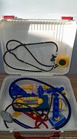 Open white plastic case showing various colorful miniature medical tools inside including stethoscope, syringe, thermometer, and scissors.