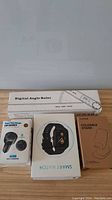 Overview photo showing all four boxed items: digital angle ruler, black smart watch, 4 USB car charger, and foldable cellphone stand.