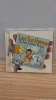 Front cover of the CD case showing the title 'Love You Forever: The Best of Robert Munsch' with child illustration and title text.