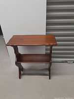 Side view of vintage wooden side table showing the magazine holder lower shelf and curved edges on the top surface.
