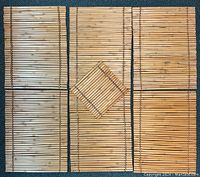 Full set of six bamboo placemats and one square trivet arranged on a dark teal carpet.
