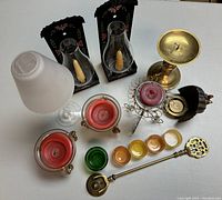 Overview of assorted candle holders including glass chimneys, brass and metal holders, small votive cups, and a brass candle snuffer.