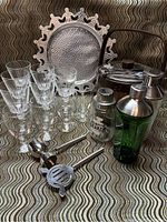 Photo of the barware lot showing nine crystal glasses, hammered metal serving tray, two cocktail shakers, metal jigger, muddler, and ice bucket with tongs.