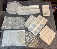 Overall layout of nine vintage doilies and linens on gray surface, showing various shapes, sizes, and textures.