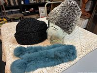 Two vintage lambswool hats and one blue dyed rabbit fur scarf displayed on a table, with a glass head for presentation (not included).