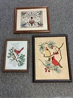 Lot of three framed needlepoint artworks placed on carpet, showing different bird themes and frames.