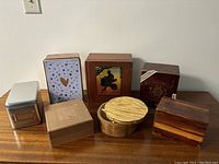 Photo showing seven assorted wooden and metal boxes arranged on a table, including cigar boxes and decorative wooden boxes.