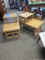View of pair of two-tier mid-century modern end or sofa tables stacked side by side showing light wood finish and geometric bases.