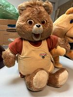 Teddy Ruxpin plush animatronic toy seated, showing detailed face and shirt with logo.