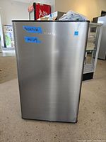 Front view of the stainless steel compact fridge with blue tape labels indicating 'Tested OK' and 'Mini Cool'.