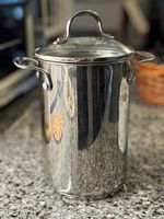 Front view of stainless steel tall pot with two side handles and glass lid on granite countertop.