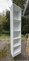 White wood bookcase standing outside with visible four shelves and adjustable shelf peg holes.