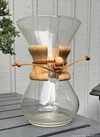 Front-side view of clear glass Chemex drip coffee carafe with wooden collar and leather tie strap, showing overall shape and condition.