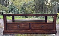 Front view of solid wood coffee table showing two drawers with metal ring handles and open shelf beneath top surface, all items in fair condition.