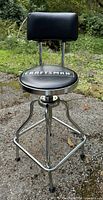 Front view of Craftsman hydraulic stool with padded black vinyl seat and backrest, chrome frame, outdoor setting.