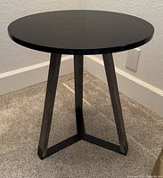 Front and side view of the small end table showing the black lacquer round top and wooden legs connected by iron accents at the base.