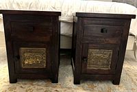 Front view of both nightstands side by side against a bed backdrop, showing matching drawers and lower cabinets with brass panels