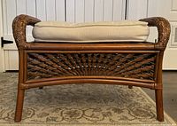 Front view of a brown rattan ottoman showing woven panel and cream cushion on top.
