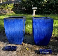 Photo of two blue glazed outdoor planters from front view showing square tapered design and pedestal pieces on the ground