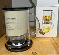 Teavana Perfectea Maker with box. Clear plastic informational insert inside the brewing chamber. The infuser has a handle and a black lid and base.