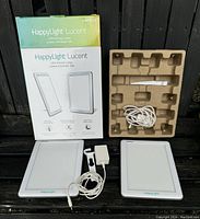Front view of two Verilux HappyLight Lucent lamps with power cables, adjustable stands, and original packaging boxes and inserts.
