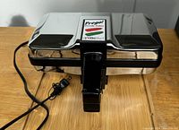 Front view of closed stainless steel and black plastic VillaWare Prego Pizzelle Baker with power cord coiled and handle in locked position.