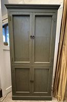 Front view of rustic avocado green wood cabinet with four closed doors and brass ring handles.