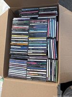 Top view photo of open cardboard box filled with over 70 CDs in jewel cases tightly packed, visible fronts and spines with varying titles and artists