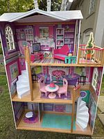 Front view of the three-story dollhouse showing living room, dining room, and bathroom with furniture inside.