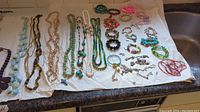 Complete overview of assortment of fashion jewelry including multiple necklaces and bracelets laid on white paper.
