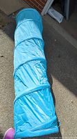 Full length view of the cylindrical blue collapsible play tunnel laid out flat on the ground.