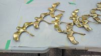 Close-up of three stylized gold bird figures on white paper backing