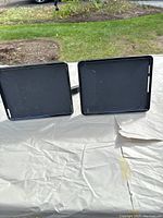 Two black rectangular device holders shown back side, made of plastic, each with adjustable grips for car mounting.