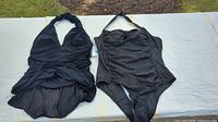 Two black halter neck one-piece swimsuits laid flat showing front and back.