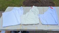 Four pairs of white bell bottom pants laid out on a table, showing different folds and sizes.