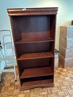 Front view of brown wood bookcase showing four shelves, one fixed solid shelf in the center, three adjustable shelves, polished finish.