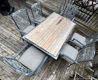 Top angle view of the entire dining set on a wooden deck, showing table and all six chairs with cushions.
