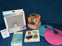 Photo showing Babymoov gray pillow, colorful Big Top Discovery Cube with attached rings, two plastic bibs (turquoise and pink), and First Signs sign language book with baby on cover.