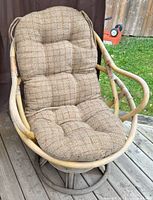 Photo of bamboo swivel rocking chair with tufted brown plaid cushion tied in place, showing chair frame and cushion details.