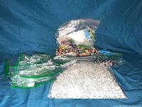 Image showing several large zip-lock bags filled with a variety of beads including white clear beads, multicolor beads, and alphabet letter beads in black and white.