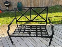 Black metal outdoor bench frame with geometric cross-back design and lattice seat base shown without cushions.