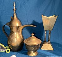 Brass coffee pot, lidded sugar bowl, and brass floral-patterned holder shown on blue background for detail.