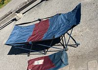 Camp cot unfolded and placed on pavement with the storage bag beside it, showing overall condition and design.