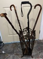 Photo showing metal cane or umbrella holder filled with four canes including three wooden and one modern black cane.