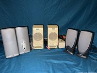 Overall photo showing four sets of computer speakers: Bose (silver), Altec Lansing (off-white), Dell (black), along with visible power adapter and cables.