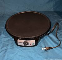 Front view of the black circular Chefman crepe maker showing the control knob and indicator lights.