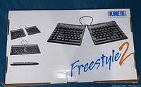 Box packaging showing the Kinesis branding and images of the split keyboard in different configurations with large 'Freestyle2' text.