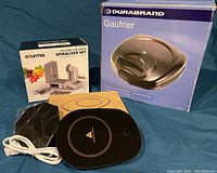 Photo showing the boxed Gourmia 5-Blades Spiralizer Set, Durabrand boxed waffle maker, and a coffee cup warmer with power supply.