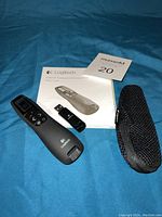 Logitech professional presenter remote, USB receiver, carrying case, and user manual displayed on blue fabric.